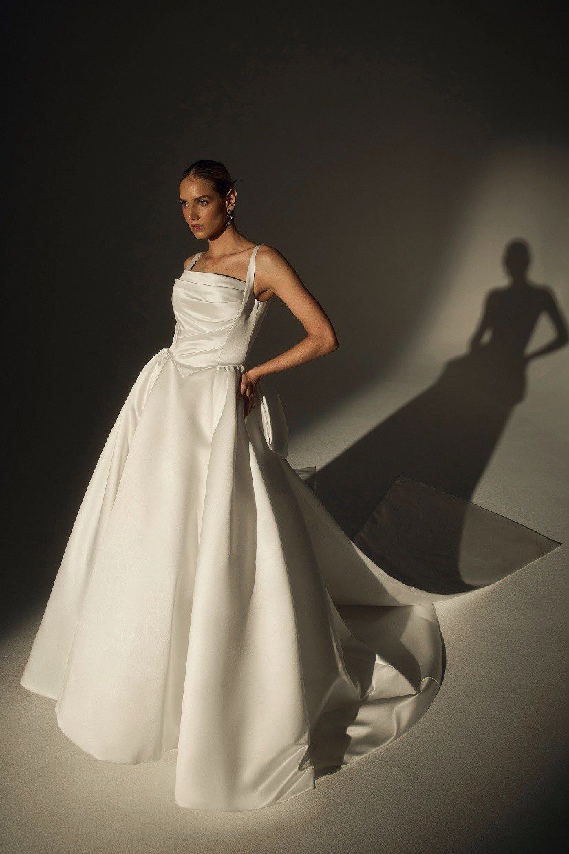 Elegant woman in a stylish white evening gown posing with a dramatic shadow.
