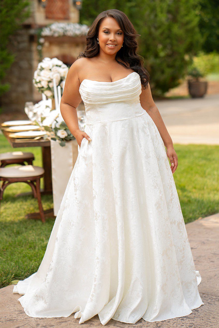 Bride in a strapless white wedding gown standing outdoors.