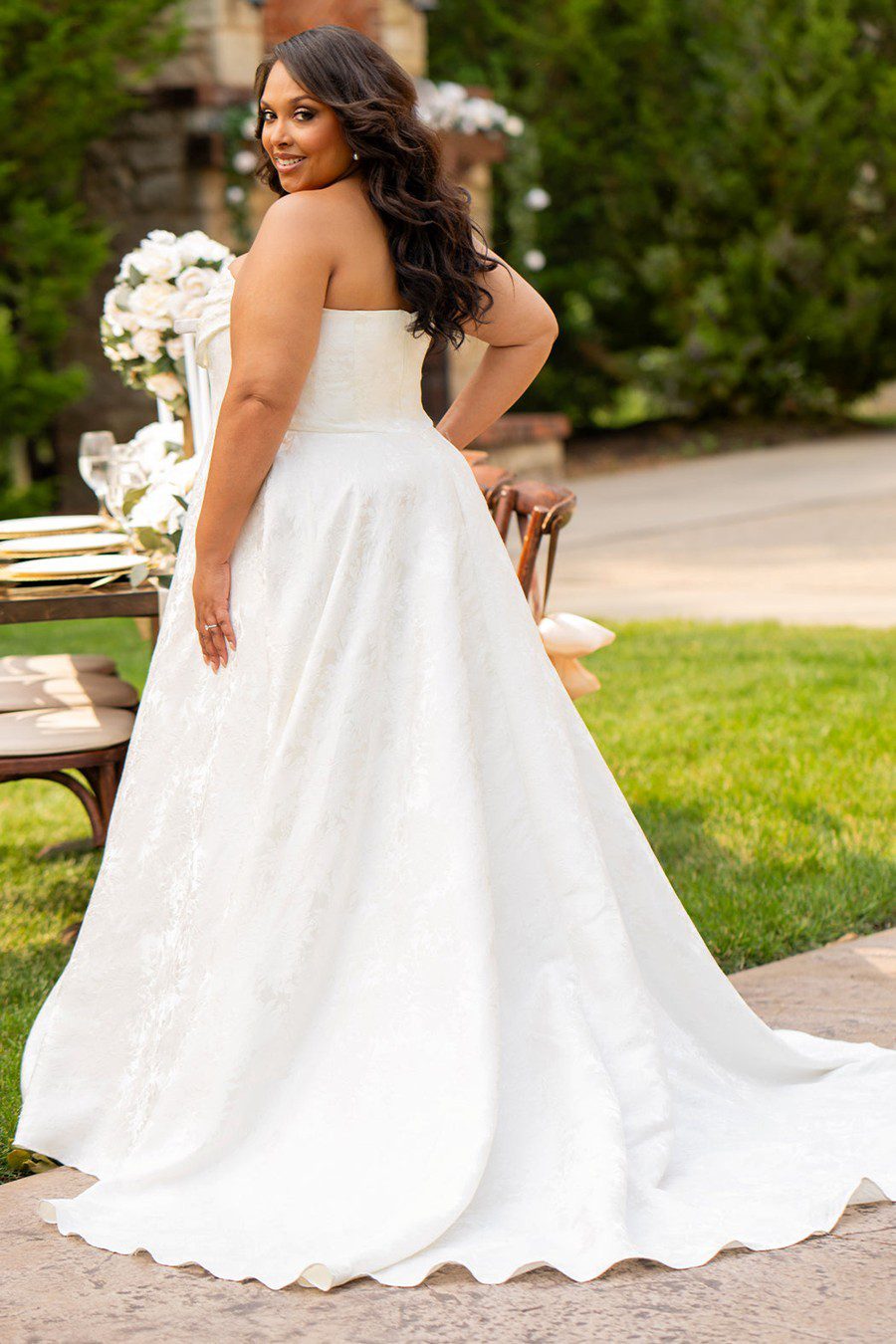 Bride in a white strapless wedding gown standing outdoors on grass.