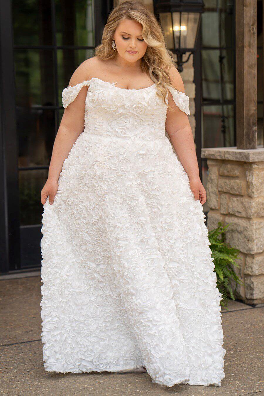 Woman wearing a white floral textured wedding dress outdoors.