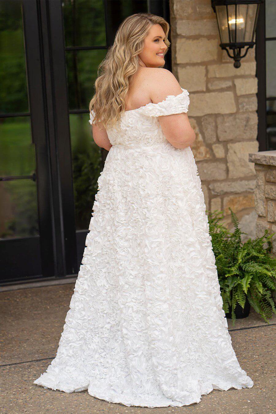 Bride in a textured white wedding gown standing outdoors near stone walls.